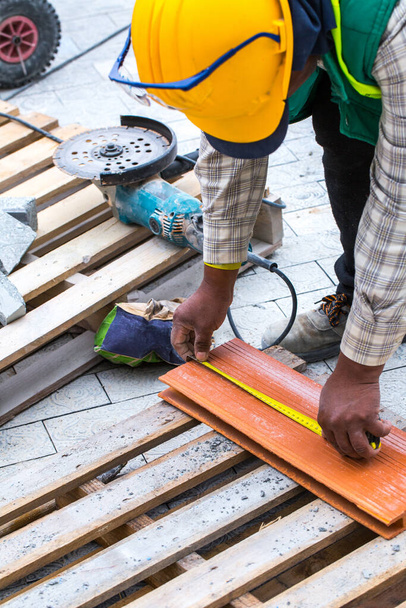 Construction work on pavement. Installation of concrete paver blocks on the sidewalk. A worker makes measurements, mark and cut build materials by a disc cutter. - Foto, afbeelding