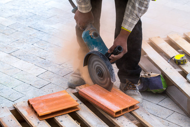 Construction work on pavement. Installation of concrete paver blocks on the sidewalk. A worker makes measurements, mark and cut build materials by a disc cutter. - Photo, Image