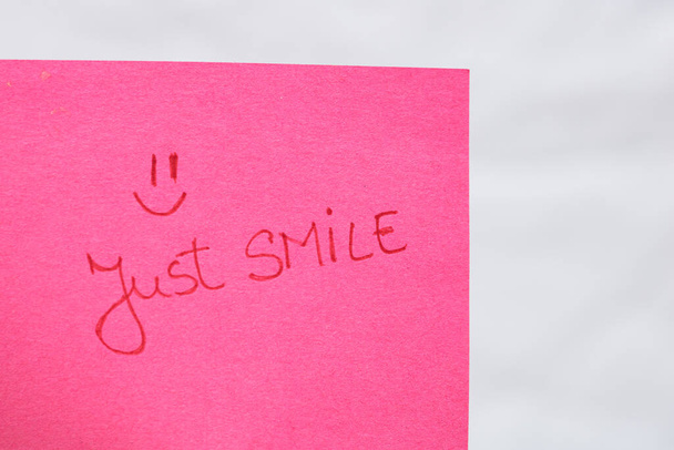 Gewoon glimlach handschrift tekst close-up geïsoleerd op roze papier met kopieerruimte. Tekst schrijven op memo post herinnering - Foto, afbeelding
