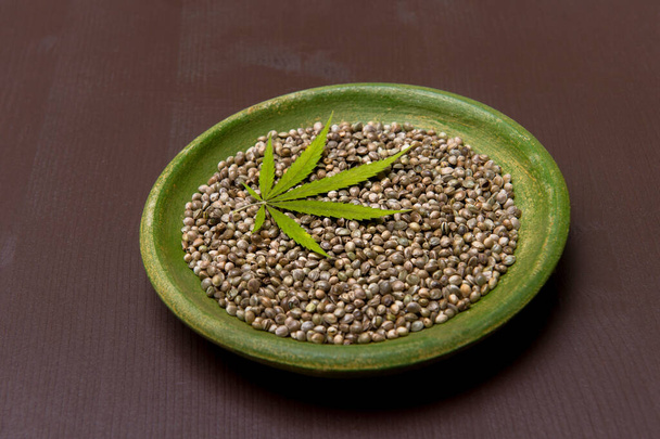 Hoja de cannabis verde y semillas en plato sobre fondo de madera. Concepto de comida vegetariana
 - Foto, Imagen