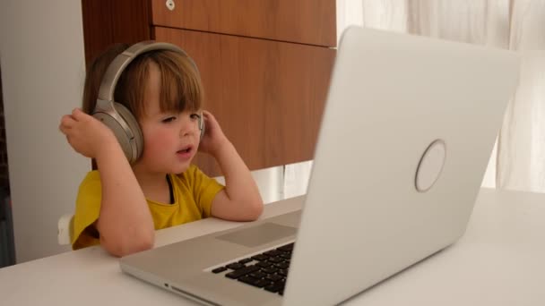 Child listens to music on headphones in front of laptop - Imágenes, Vídeo