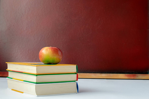 There are books with an apple on the table. Against the background of a school board. Symbolizes schooling. Horizontal frame . - Photo, Image