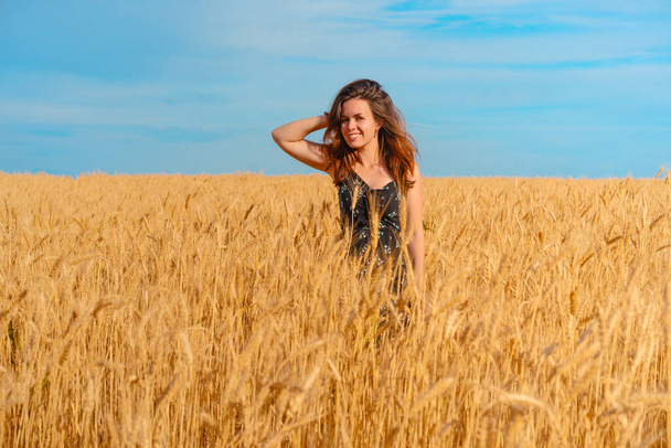 Een mooie jonge vrouw met lang haar staat in een tarweveld, een plek voor tekst en zonneschijn - Foto, afbeelding