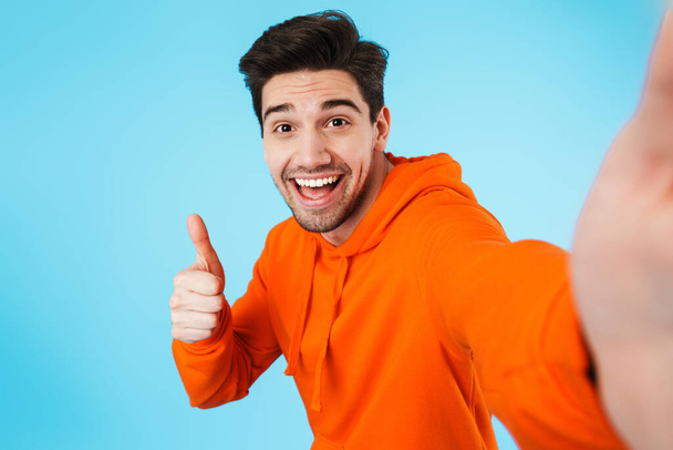 Image of happy young bristle man isolated over blue wall background take a selfie by camera showing thumbs up. - Foto, immagini