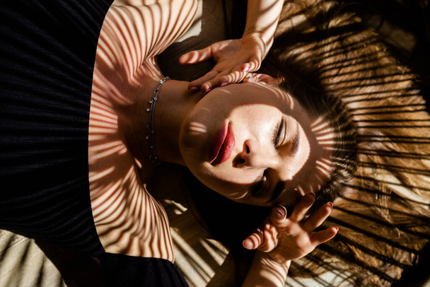 Retrato de mulher bonita com sombras de folha de palmeira em seu rosto. Conceito de banho de sol, férias
. - Foto, Imagem