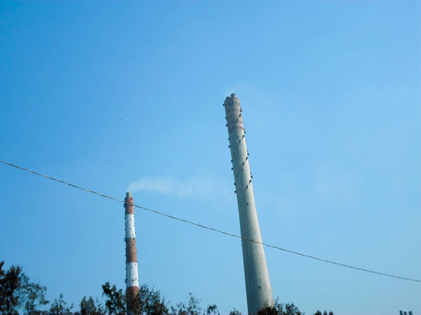Заводские дымовые трубы излучают дым, промышленные дымовые трубы, дымовые трубы высокой промышленной фабрики дымовые трубы вентиляции, чтобы выпустить дым и пар изолированы на фоне голубой атмосферы неба. Копирование пространства - Фото, изображение