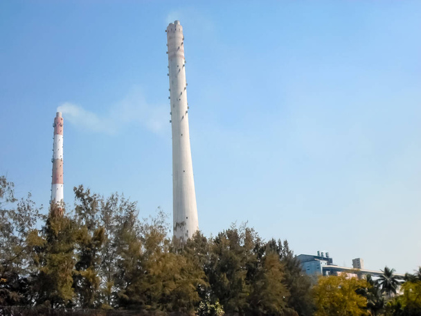 Factory chimney emits smoke, industrial smoke chimneys, Tall industrial factory chimney smokestacks ventilation to release smoke and steam Isolated against blue sky atmosphere background. Copy space - Photo, Image