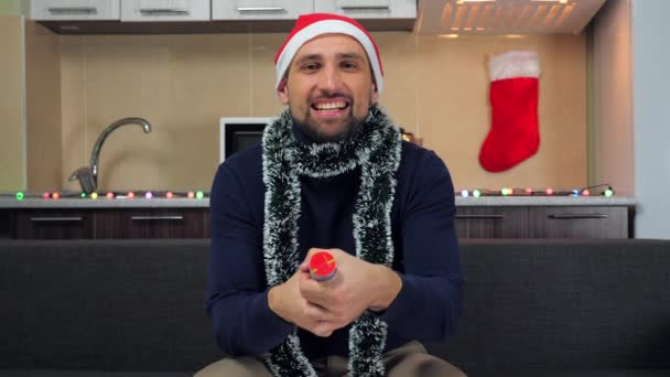 Uomo positivo a Capodanno cappello rosso Babbo Natale, esplode cannone coriandoli, sorride - Filmati, video