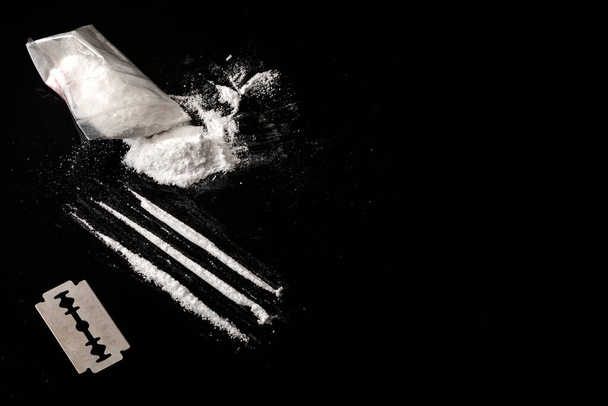 Narkomania i nadużywania substancji motyw koncepcyjny z linii kokainy, mała torba z białym proszkiem i ostrze używane do cięcia każdej linii narkotyków na ciemnym lustrzanym stole z miejsca kopiowania - Zdjęcie, obraz