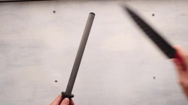 Το χέρι του λευκού ανθρώπου ακονίζει ένα μαχαίρι κουζίνας με ένα χάλυβα λείανσης σε ένα λευκό φόντο πίνακα - Πλάνα, βίντεο