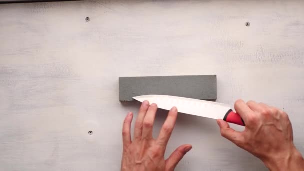 Білий чоловік наточує кухонний ніж на прямокутний камінь - Кадри, відео
