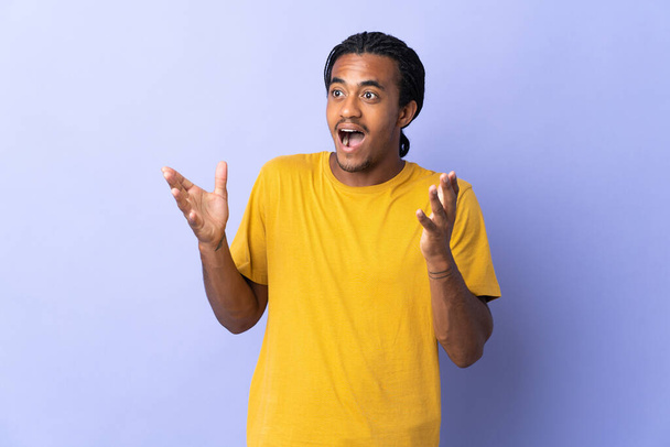Jovem afro-americano com tranças homem isolado no fundo roxo com expressão facial surpresa
 - Foto, Imagem
