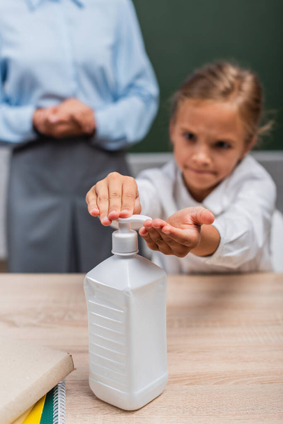 selectieve focus van schoolmeisje toepassen van antiseptische op handen in de buurt van leraar - Foto, afbeelding