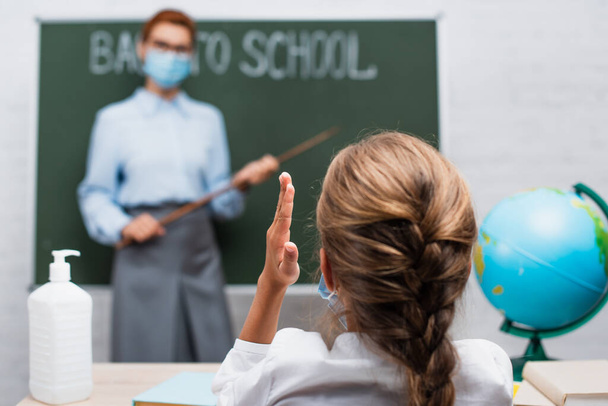 back view of schoolgirl with raised hand, and teacher with pointing stick near chalkboard  - Zdjęcie, obraz