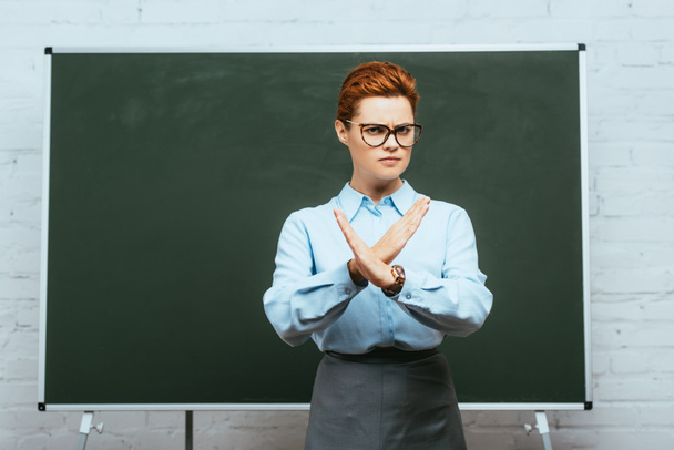 serious teacher in eyeglasses showing stop gesture while standing near chalkboard - Photo, image