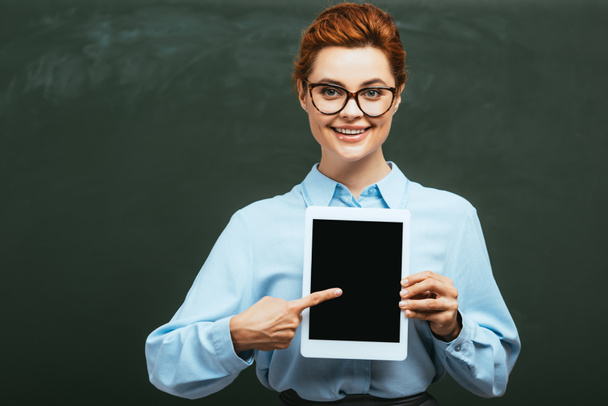zufriedener Lehrer zeigt mit dem Finger auf digitales Tablet mit leerem Bildschirm in der Nähe der Tafel - Foto, Bild