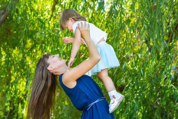 Mother plays with her daughter in the park. Throws up the child. mom and daughter laugh - Foto, Bild