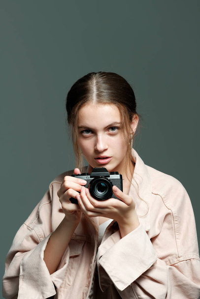A girl photographer in a pink jacket holds a mirrorless camera in her hands. - Foto, Imagem