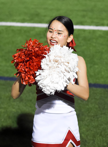 Schattig Aziatisch Amerikaans cheerleader presteren op een middelbare school voetbal spel - Foto, afbeelding