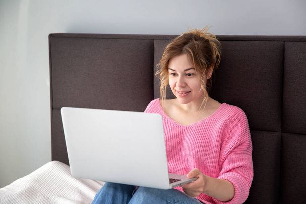  Kaunis tyttö istuu vaaleanpunaisessa puserossa kannettavan tietokoneen kanssa, juttelemassa.  - Valokuva, kuva