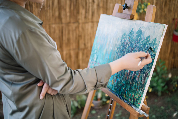 Female hand holding paintbrush and painting on canvas - Фото, изображение