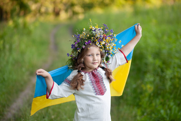 Ουκρανία κυματίζει μπλε και κίτρινη σημαία στα χέρια του μικρού Ουκρανού κοριτσιού. Χαμογελαστό παιδί με παραδοσιακό κέντημα (vysyvanka). Ημέρα Ανεξαρτησίας της Ουκρανίας. Ημέρα σημαίας - Φωτογραφία, εικόνα