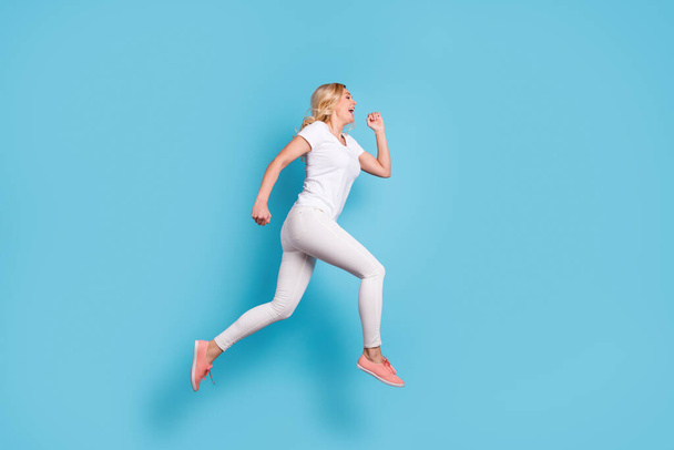 Full length profile photo of attractive funny crazy lady jump high up running speed rushing shopping center wear casual white s-shirt pants footwear isolated blue color background - Foto, Bild