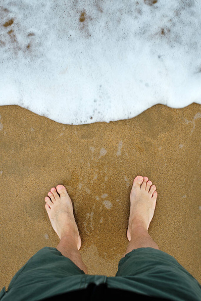 Grote voeten aan de kust van het strand wachtend op een golf - Foto, afbeelding
