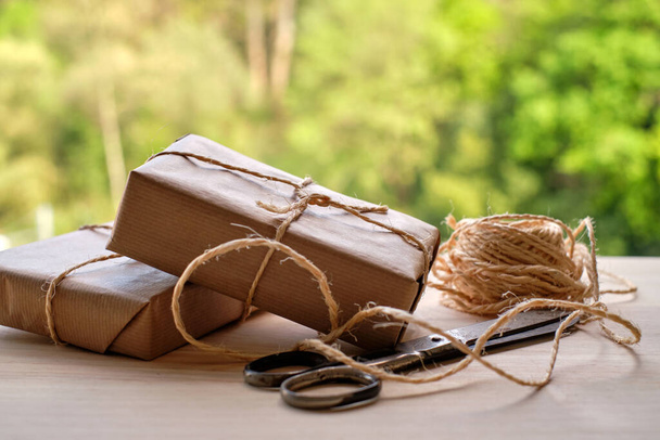 Emballages cadeaux enveloppés dans du papier kraft sur table en bois et fond de forêt - Photo, image