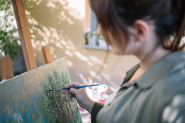Blurred brunette woman painting picture in yard - Фото, зображення