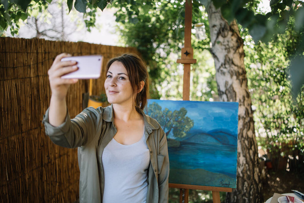 Pretty girl posing in front of painted canvas and taking selfie - Фото, зображення