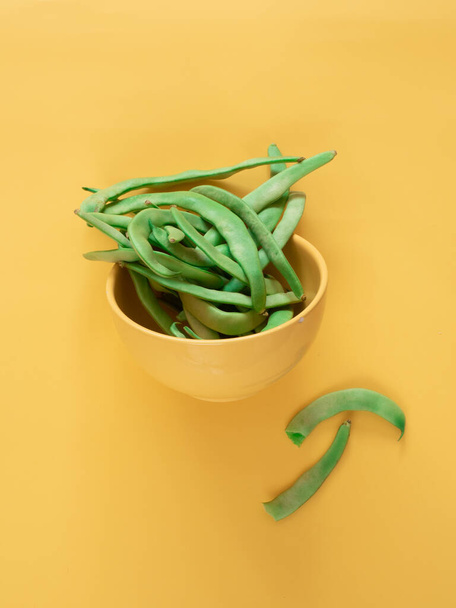 Green beans in a bowl on yellow background with copy space - Фото, изображение
