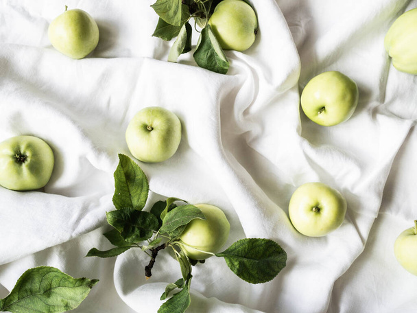 Komposition aus frischen grünen Äpfeln und Blättern auf weißer Leinenserviette. Tapete aus Früchten. Draufsicht, flache Lage. - Foto, Bild