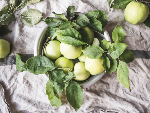 Metal bowl with green apples and leaves on a gray vintage linen napkin. Wallpaper of fruits.Top view, flat lay. - Foto, Bild
