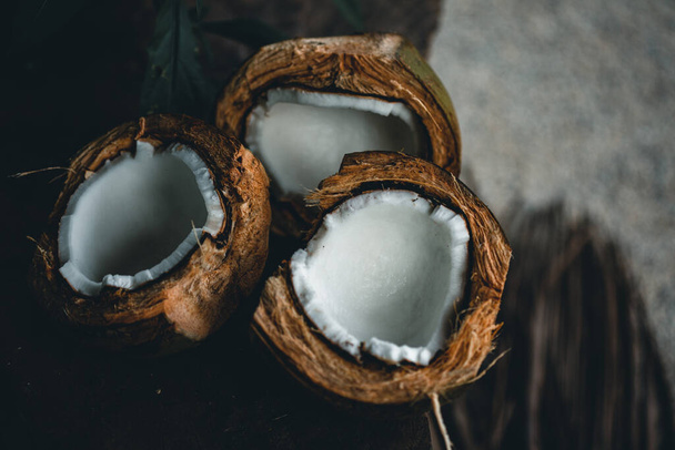 Broken coconuts on a wooden table with palm leaves close up - Foto, Imagem