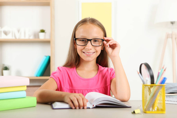 Κοριτσάκι με γυαλιά που διαβάζει ένα βιβλίο στο σπίτι. - Φωτογραφία, εικόνα