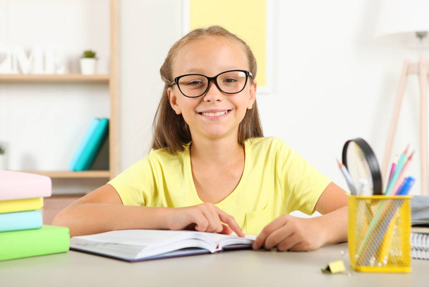 Menina com óculos lendo um livro em casa
 - Foto, Imagem