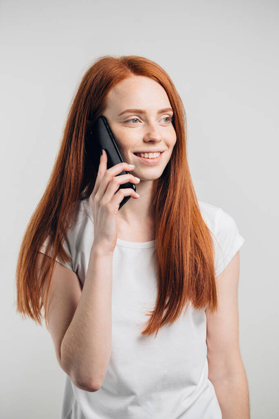 Blisko uśmiechnięta atrakcyjna dziewczyna z długimi włosami rozmawiająca przez telefon komórkowy - Zdjęcie, obraz