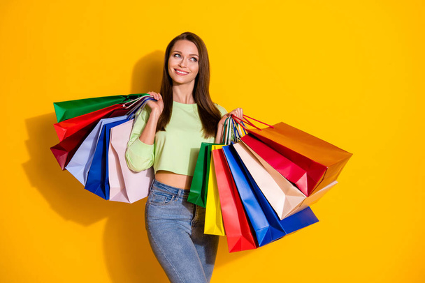 Photo of charming pretty lady good mood hold many shopping bags dream more sales wear green cropped sweatshirt jeans isolated vivid bright yellow color background - Foto, Imagem