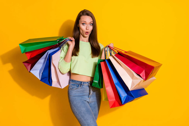 Photo of charming shocked lady good mood street look hold many shopping bags open mouth sales wear green cropped sweatshirt jeans isolated vivid bright yellow color background - Zdjęcie, obraz