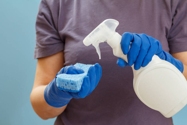 Mujer con una camiseta sosteniendo una botella de plástico de líquido de lavado y una esponja sobre el fondo azul. Concepto de lavado y limpieza
. - Foto, Imagen