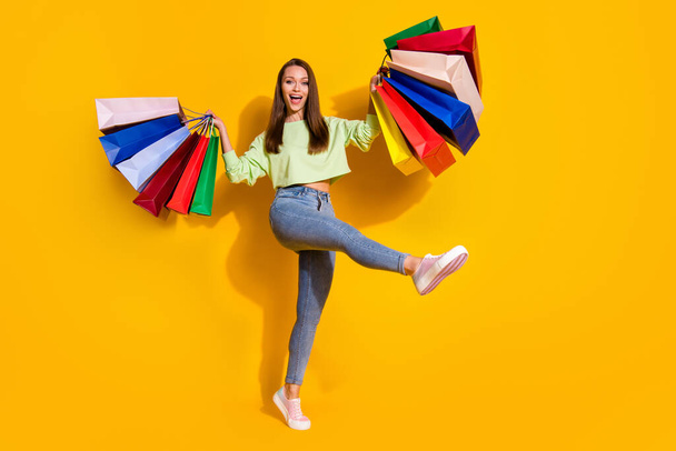 Full size photo of positive cheerful girl enjoy shopping buy many off-sales hold bags wear green good look clothes sneakers isolated bright shine yellow color background - Photo, Image