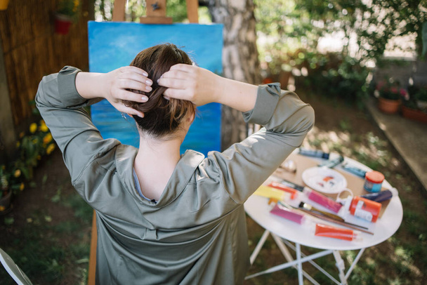 Widok z tyłu kobiety podejmowania bułki włosów w podwórku z malarstwem - Zdjęcie, obraz