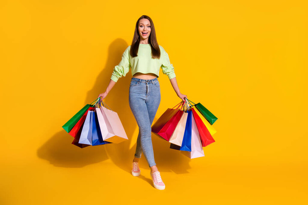 Full size photo of positive cheerful girl enjoy shopping off-sales hold many bags wear good look clothes sneakers isolated over bright shine yellow color background - Foto, Bild
