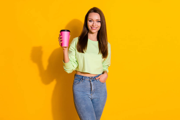 Photo of attractive lady good mood street look drink takeout coffee beverage pink cup wear green cropped sweatshirt jeans isolated vivid bright yellow color background - Foto, immagini