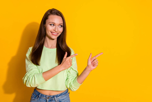 Photo of attractive lady good mood direct fingers side empty space showing novelty product wear green cropped sweatshirt jeans isolated vivid bright yellow color background - Foto, Imagen