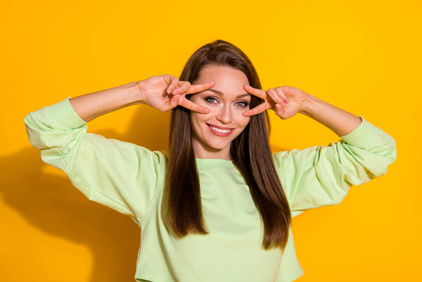 Photo of attractive pretty funny lady good mood arms showing v-sign symbols near eyes flirty wear cropped sweatshirt green sweater isolated vivid bright yellow color background - Foto, Bild