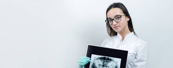 Fille dentiste dans un manteau blanc tient un instantané des dents du patient
. - Photo, image