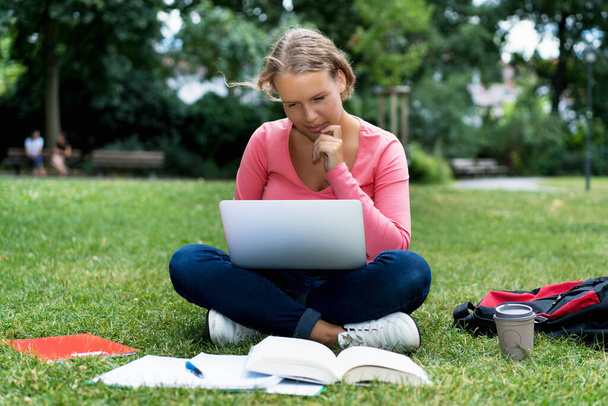 Young german female student at computer learning and preparing for degree outdoor in park on campus of university - Foto, Imagem