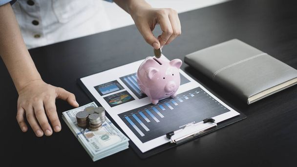 Businessman's hand holds the money in the piggy bank for saving money for future use, saving money for finance accounting concept. - Photo, Image